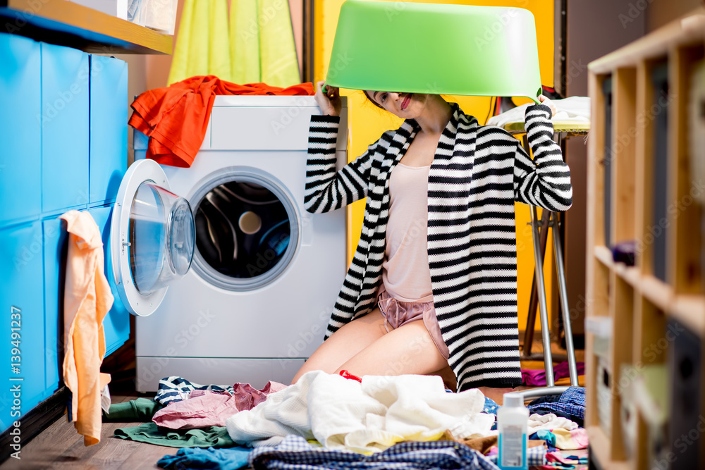 Young housewife sitting with clothes basket near the washing machine at home