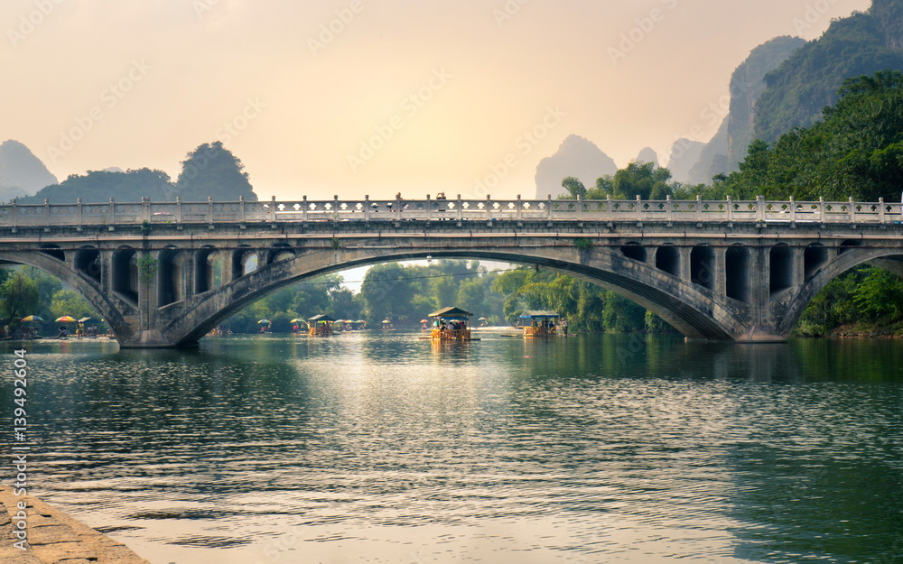 YANGSHUO, CHINA - SEPTEMBER 23, 2016: Boats with tourists floating on Li River, below a stone bridge