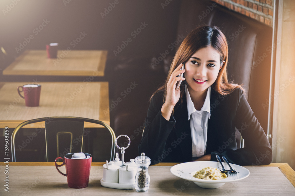 美丽的亚洲女孩在餐厅用智能手机等待时间