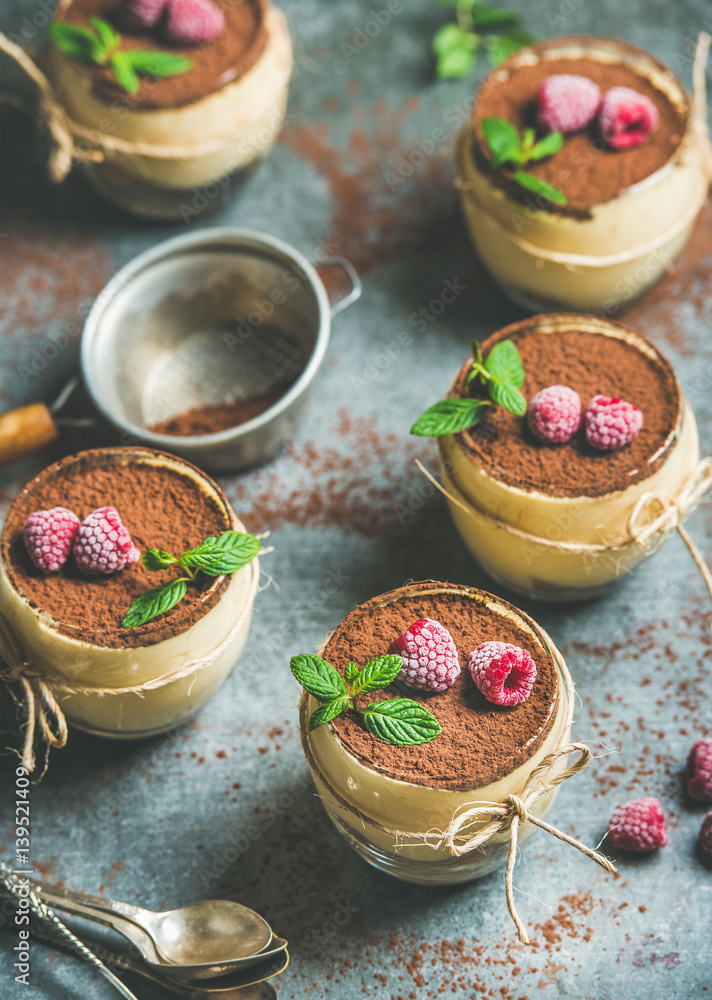 Homemade Italian dessert Tiramisu served in individual glasses with mint leaves, raspberries and coc