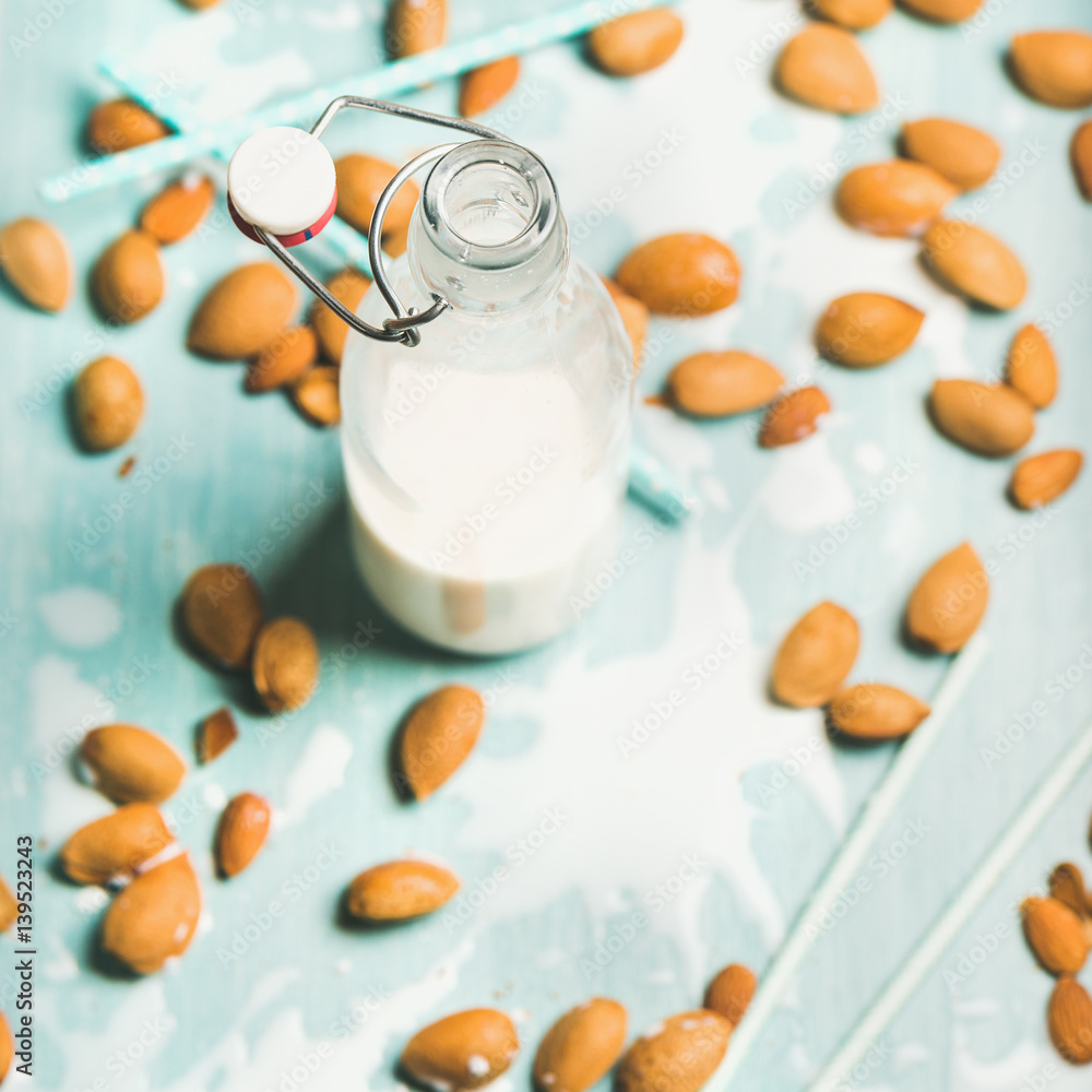 Dairy alternative milk. Almond milk in bottle and fresh nuts over blue background, selective focus, 