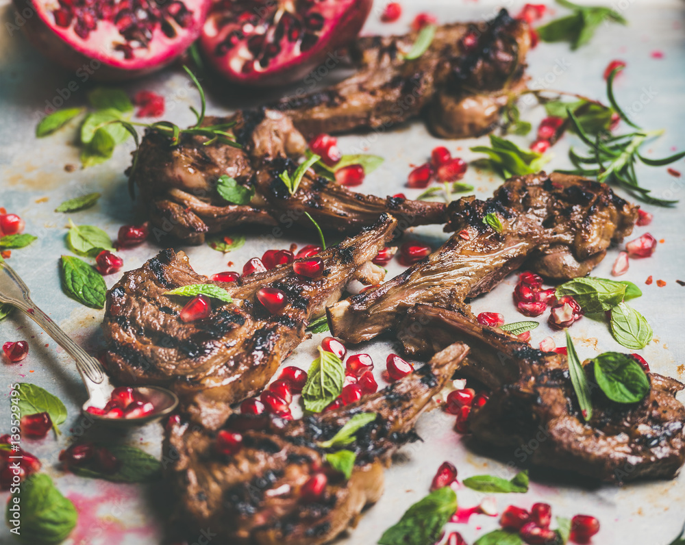 Grilled lamb ribs with pomegranate seeds, fresh mint and rosemary in metal baking tray. Meat barbecu