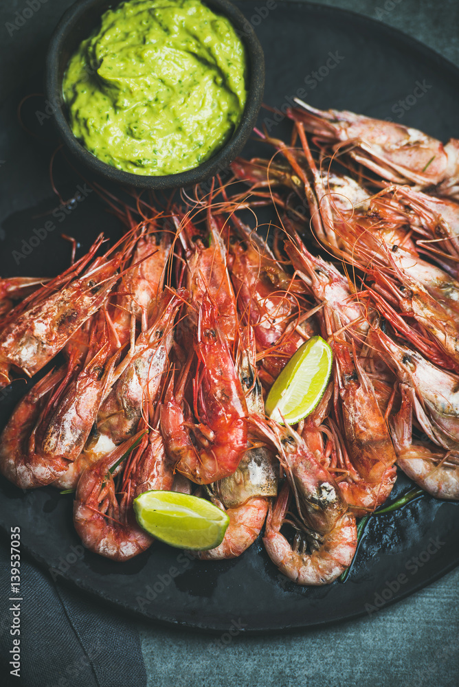 Roasted red shrimps with guacamole avocado sauce and lemon in slate stone black plate over grey conc