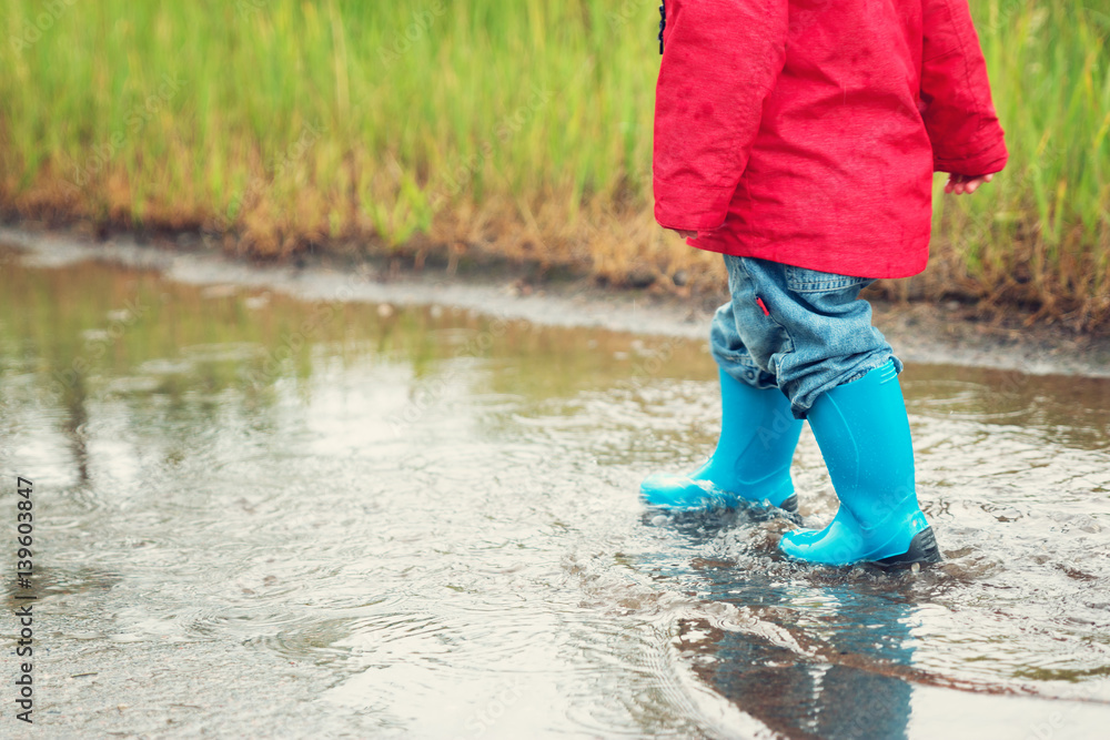 Child walking in wellies in puddle on rainy weather