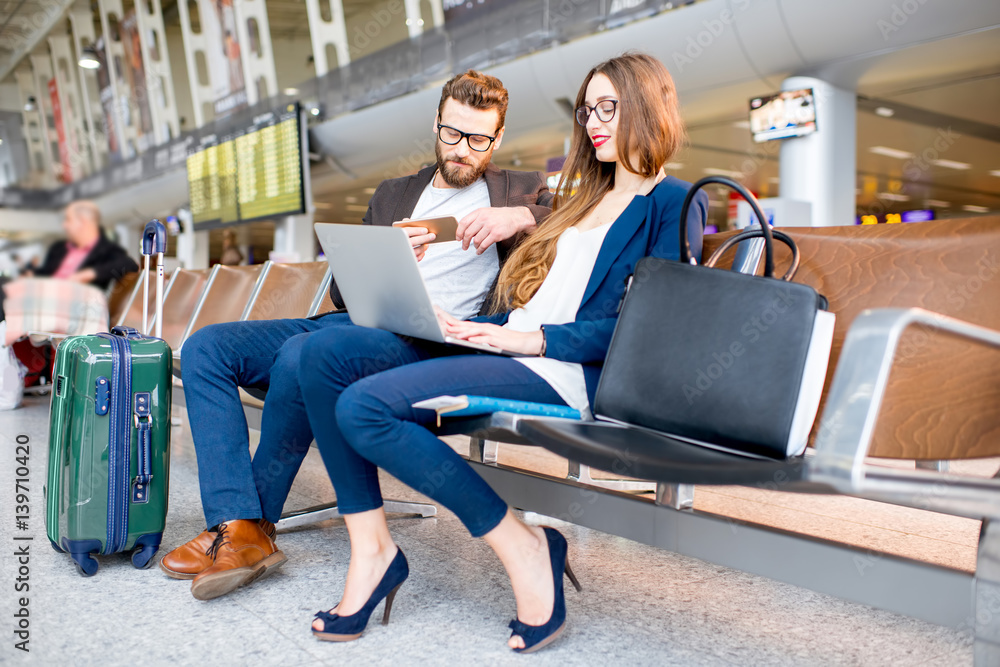 Elegant business couple working with laptop and phone sitting at the waiting hall in the airport. Bu