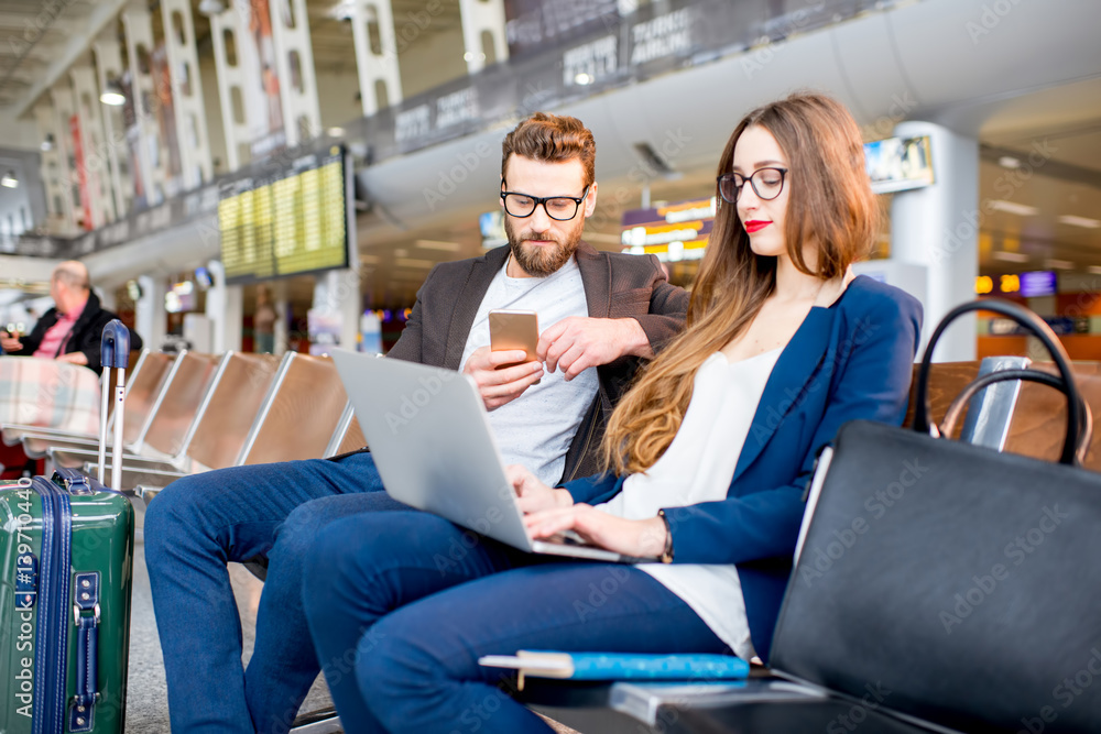 Elegant business couple working with laptop and phone sitting at the waiting hall in the airport. Bu