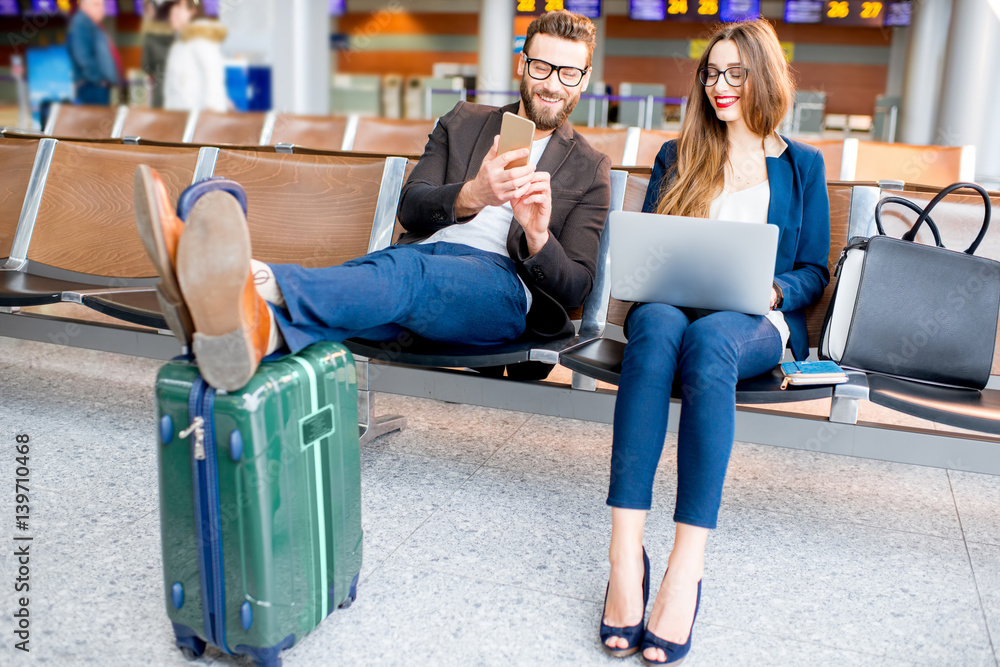 Elegant business couple working with laptop and phone sitting at the waiting hall in the airport. Bu