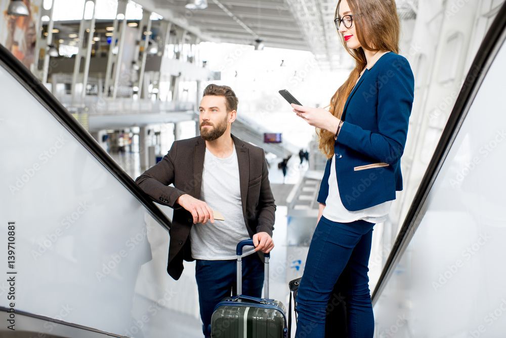 Business couple getting up with baggage on the escalators at the airport. Business travel concept