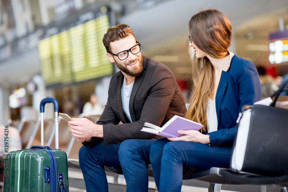 Elegant business couple sitting with phone and book at the waiting hall in the airport. Business tra