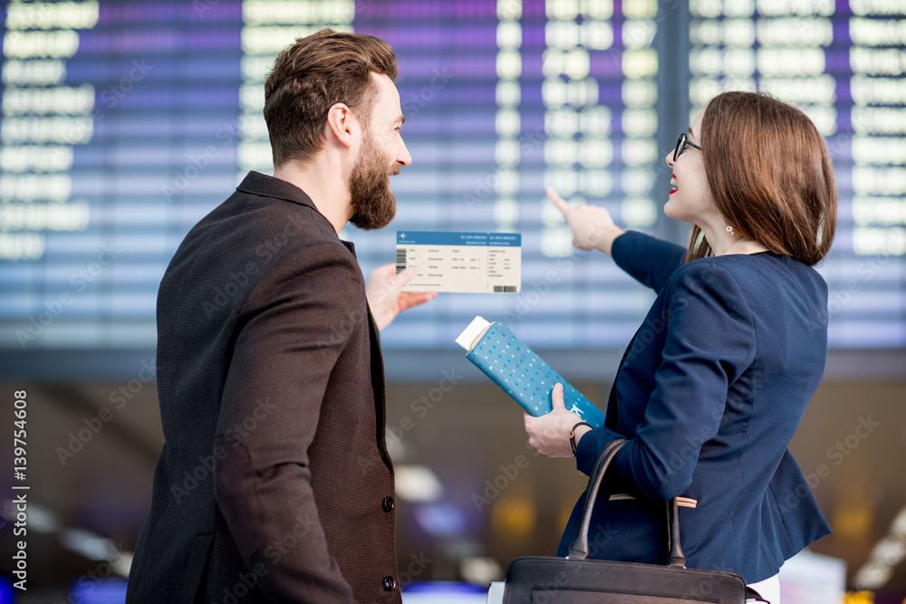 Business couple looking at the timetable holding boarding pass at the airport