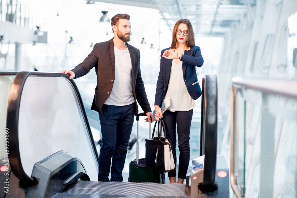 Business couple with baggage checking time getting up on the escalator at the airport