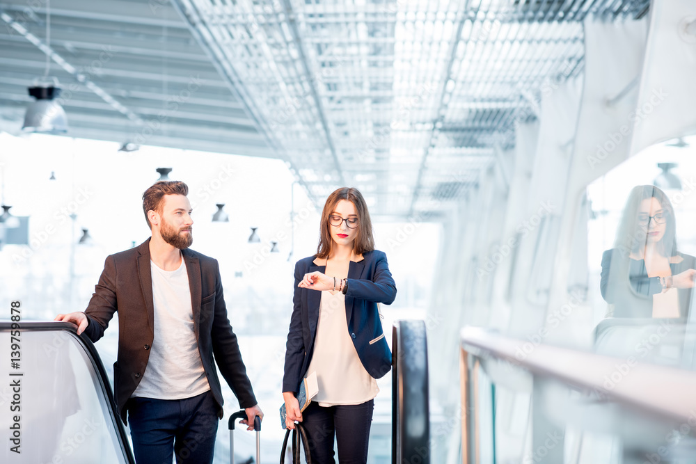 Business couple with baggage checking time getting up on the escalator at the airport