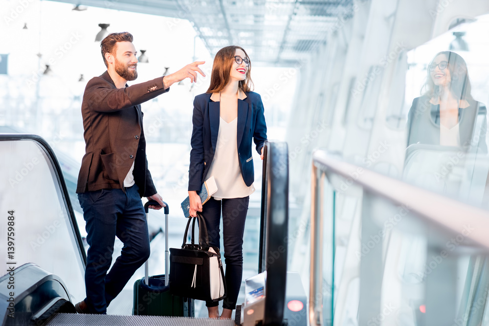 Elegant business couple with baggage getting up on the escalator to the departure area at the airpor