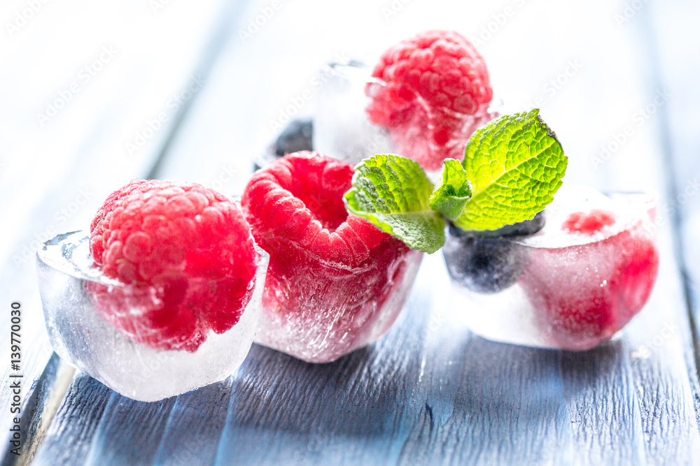 fresh berries with mint in ice cubes on wooden background