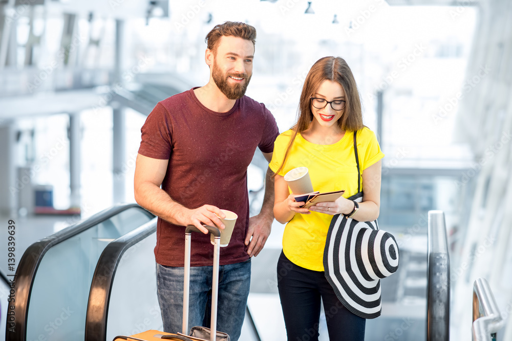 Young happy couple getting up with baggage on the escalator to the departure area of the airport dur