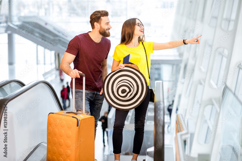 Young happy couple getting up with baggage on the escalator to the departure area of the airport dur