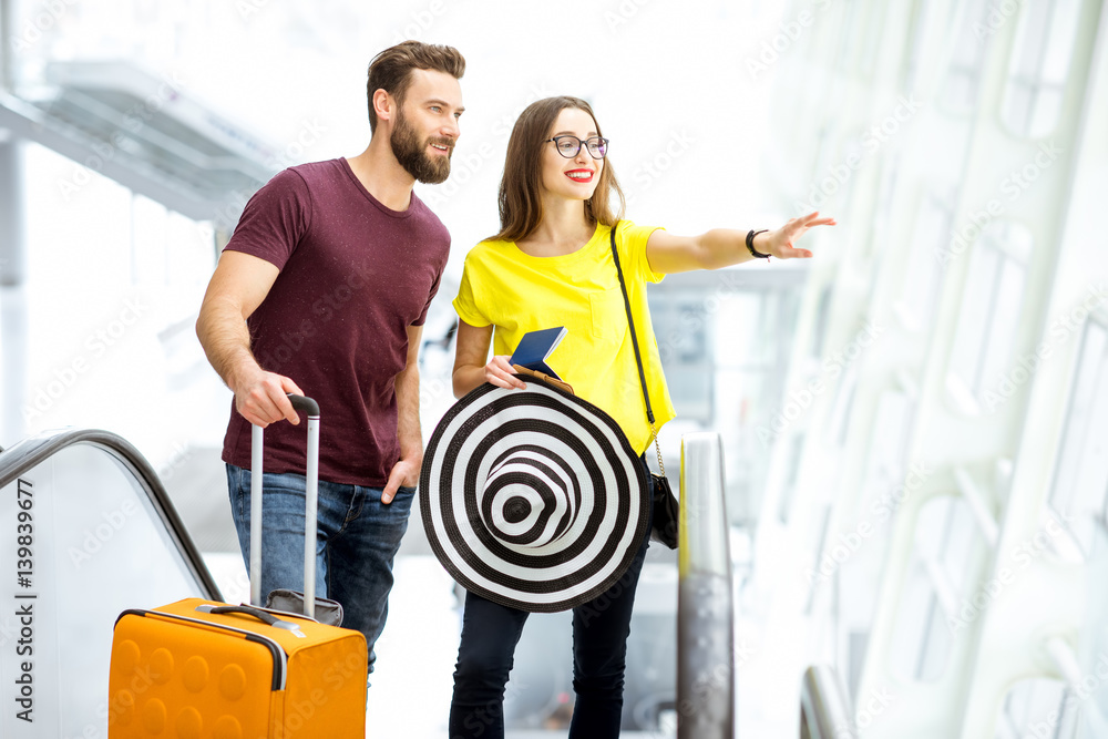 Young happy couple getting up with baggage on the escalator to the departure area of the airport dur