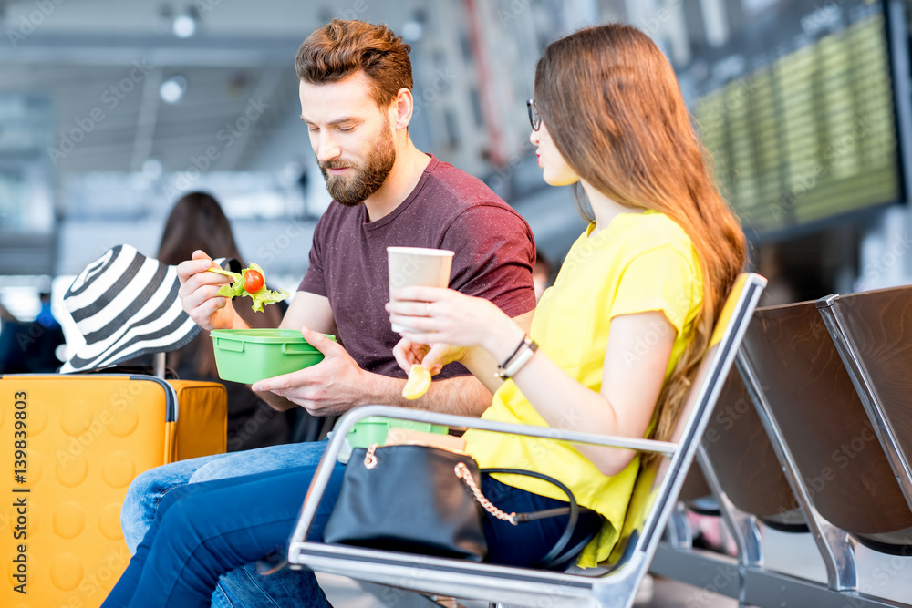 Young couple having a snack with lunch boxes at the waiting hall of the airport during their vacatio