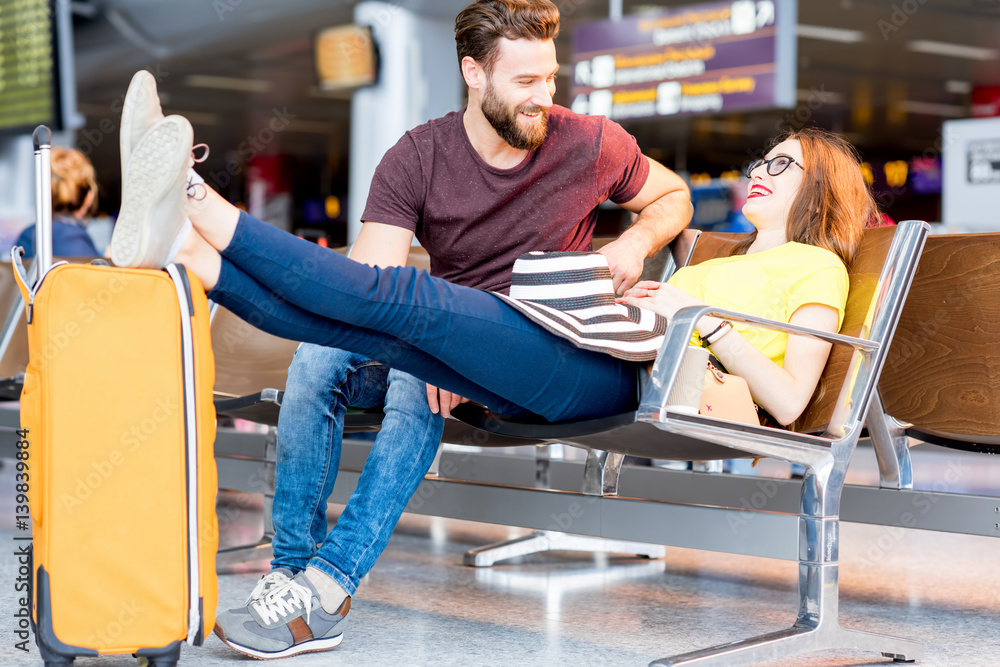 Young couple in colorful t-shirts sitting with baggage at the waiting room of the airport