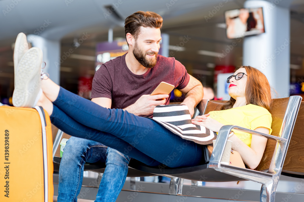 Young couple in colorful t-shirts sitting with baggage at the waiting room of the airport