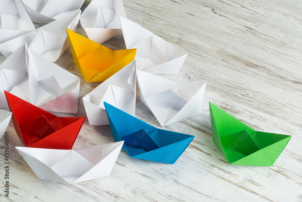 Business leadership concept with white and color paper boats on wooden table