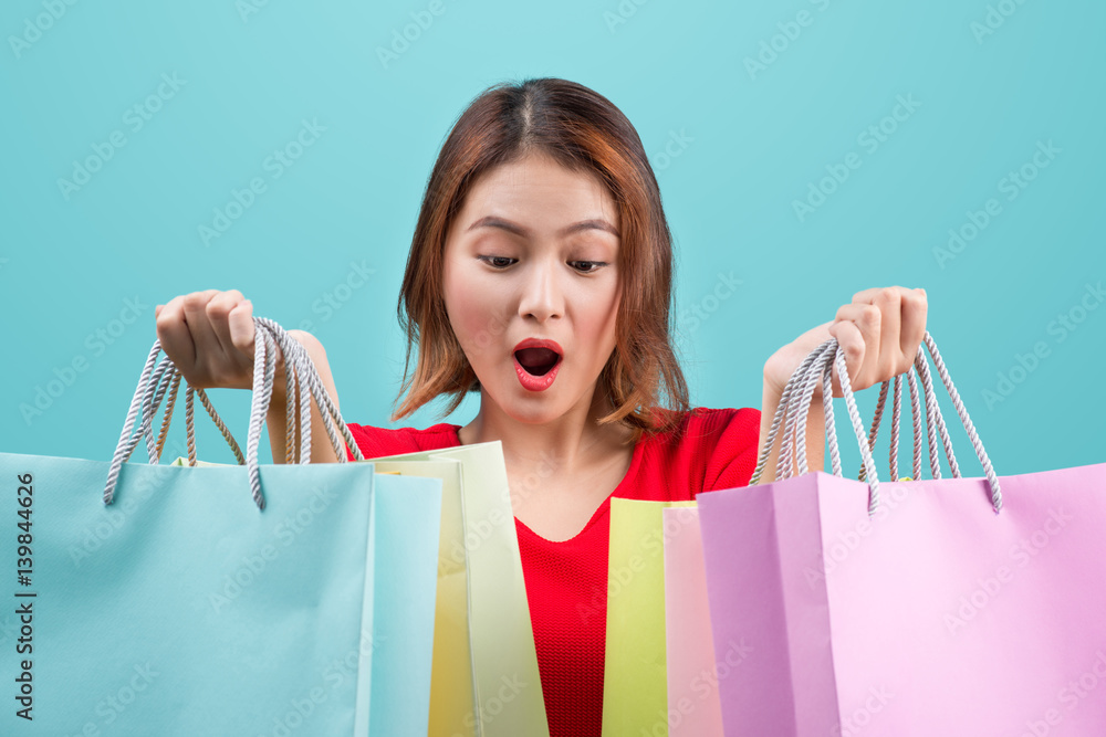 Beautiful young asian woman with colored shopping bags over blue background