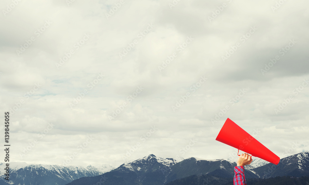 Hand of woman holding paper trumpet against natural landscape background