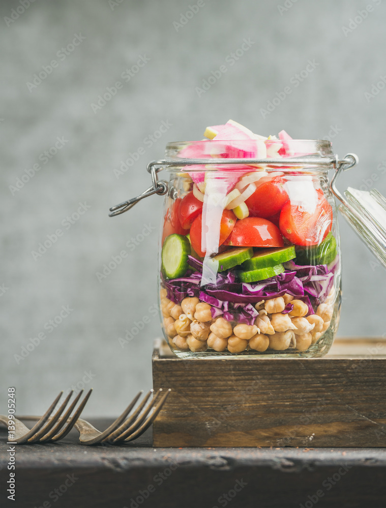 Healthy take-away lunch jar. Vegetable and chickpea sprout layered vegan salad in glass jar, grey co