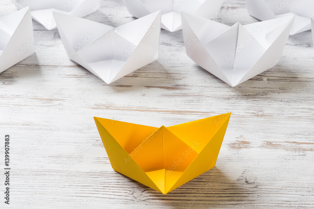 Business leadership concept with white and color paper boats on wooden table