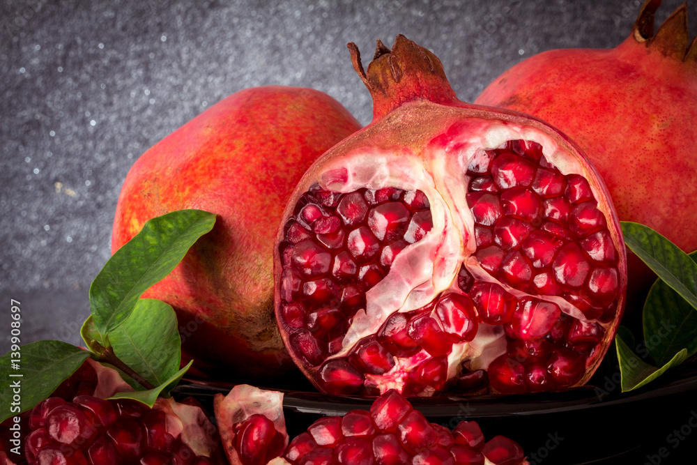 Fresh red pomegranate and seed  with leaves over black stone background