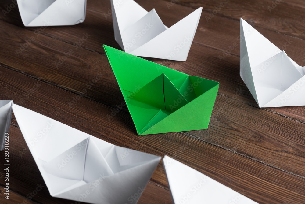 Business leadership concept with white and color paper boats on wooden table