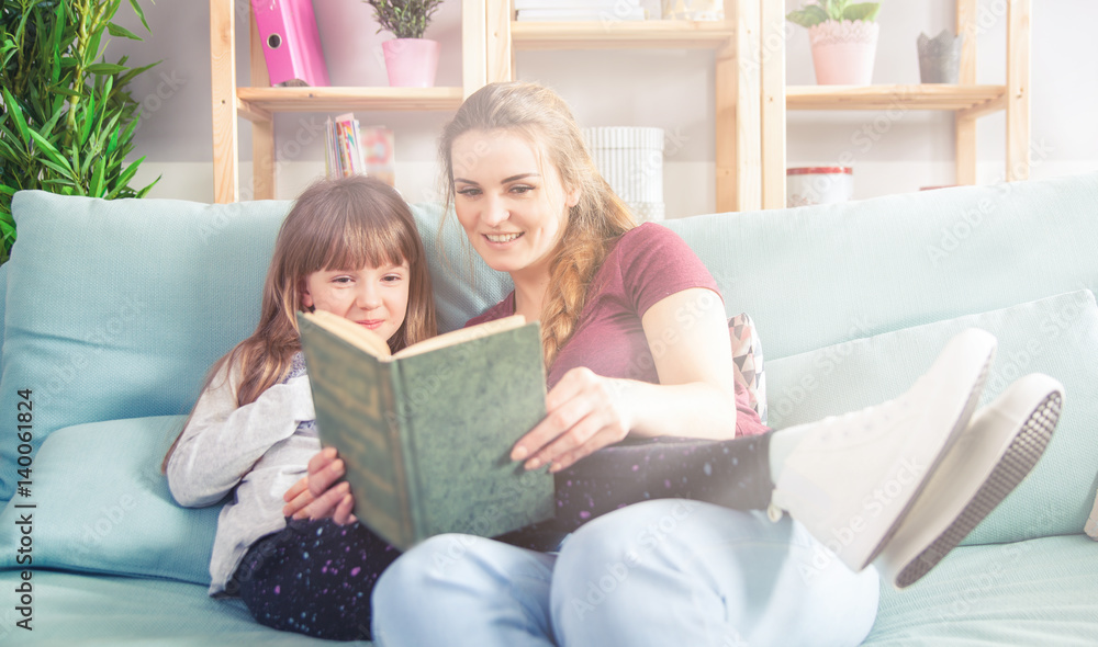 Mother and daughter sitting on sofa and reading book together