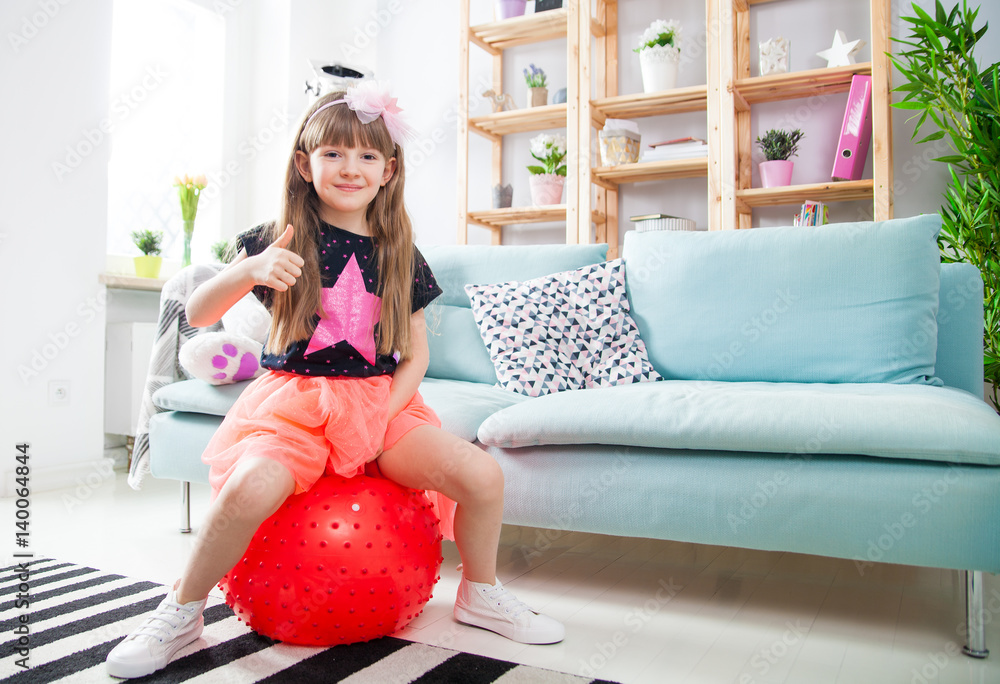 Happy child girl playing with fitness ball at home