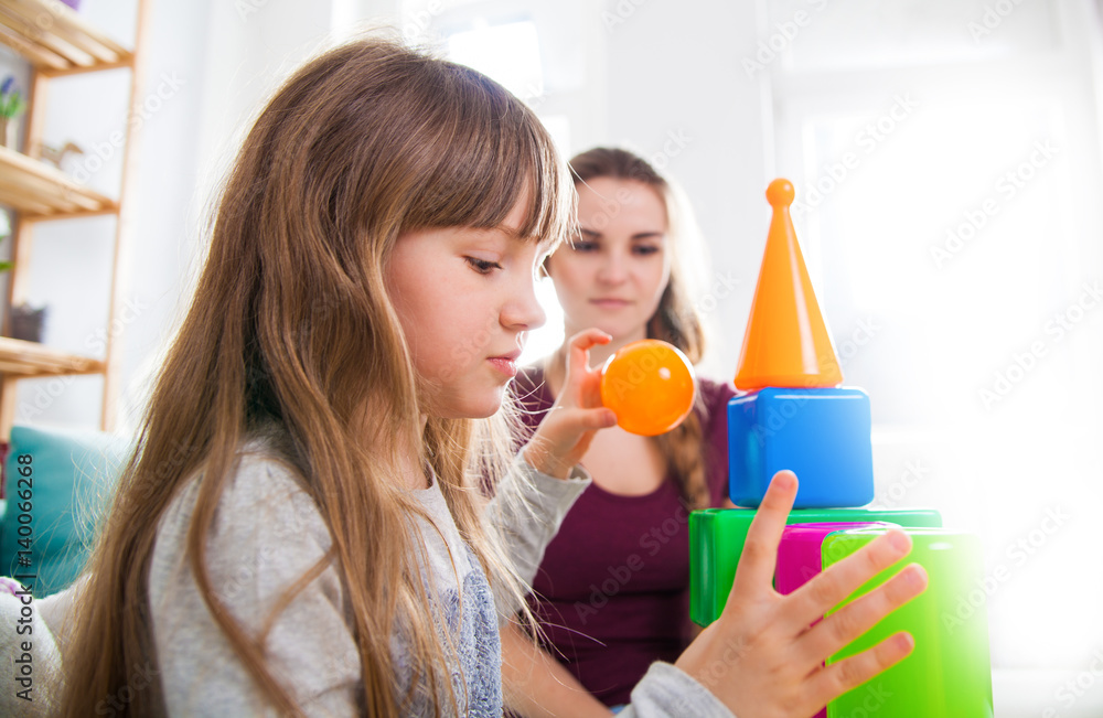 Cute little girl and her mother playing with blocks together, family at home