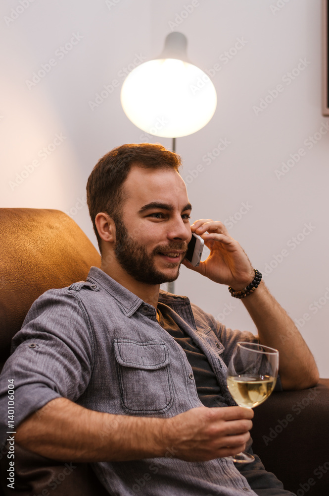 年轻的成功人士在家边打手机边喝白葡萄酒