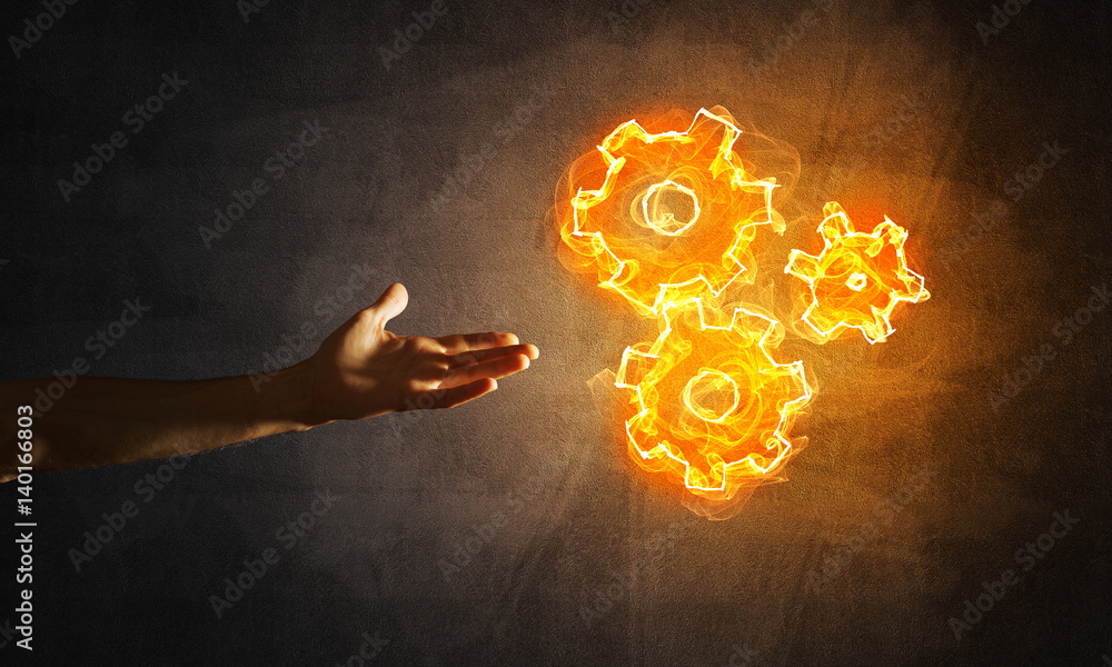 Concept of teamworking or organization presented by hands in touch and fire glowing cogwheels