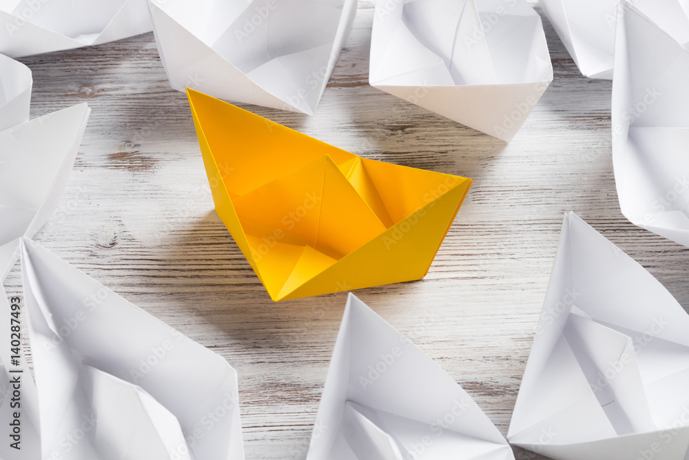 Business leadership concept with white and color paper boats on wooden table