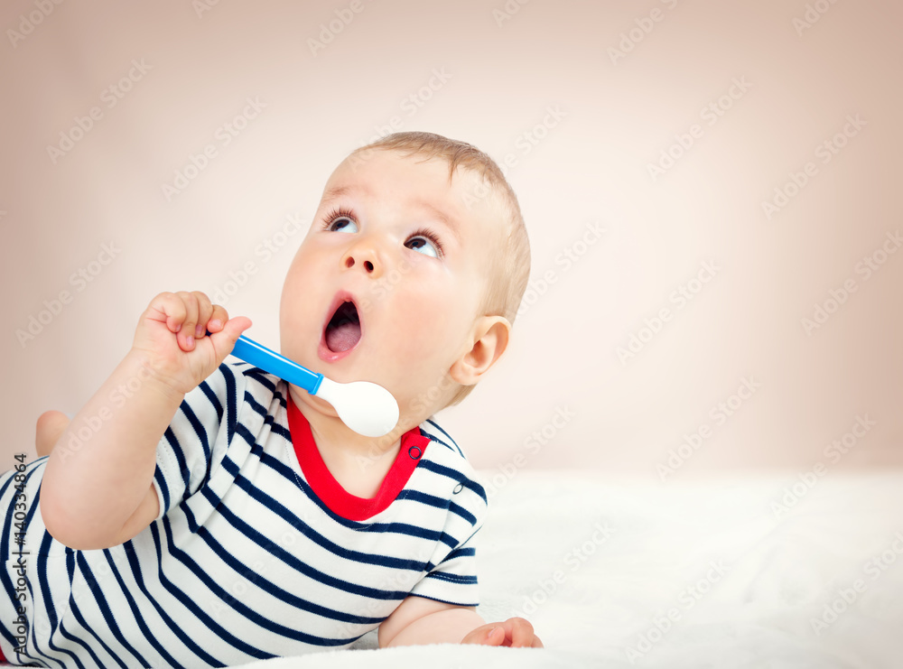 Nine month old baby lying in the bed with spoon