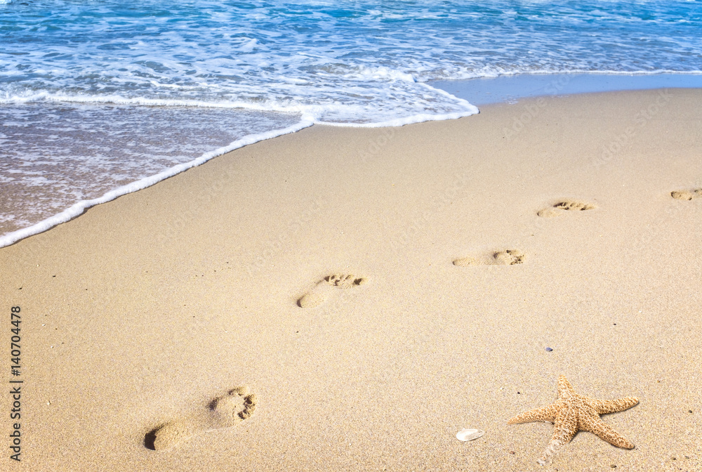 Fußspuren im Sand an einem goldenen Strand mit Seestern am Meer