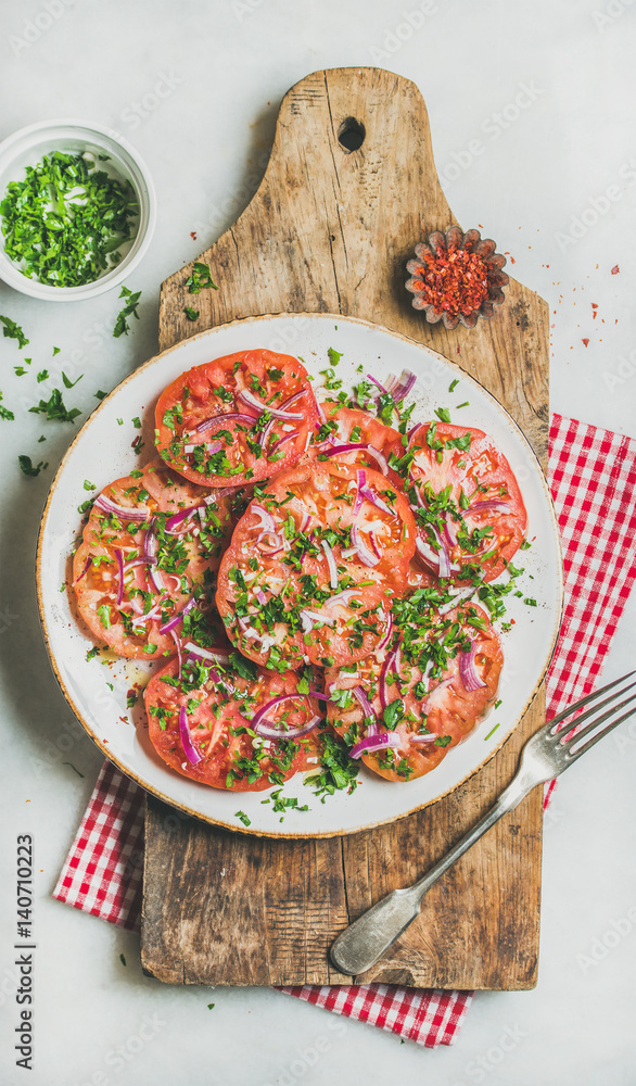 Fresh heirloom tomato, parsley and onion salad in white plate on shabby wooden board over light grey