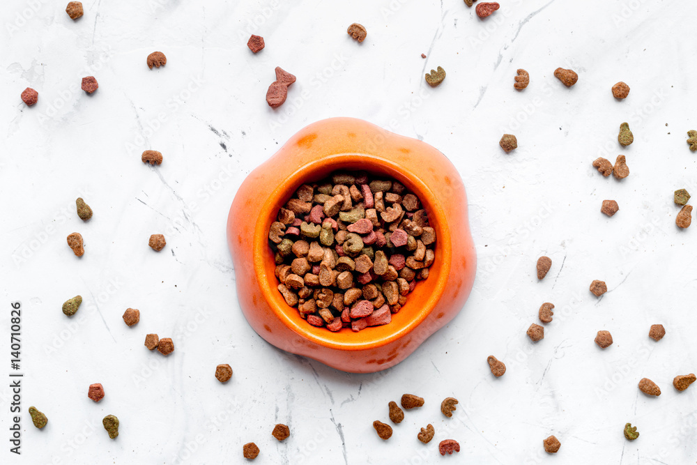 dry cat food in bowl on stone background top view