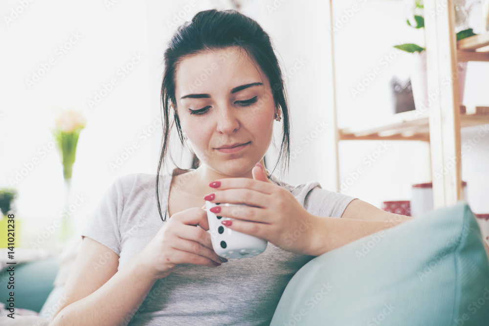 Young relaxed woman drinking coffee while sitting on comfortable sofa