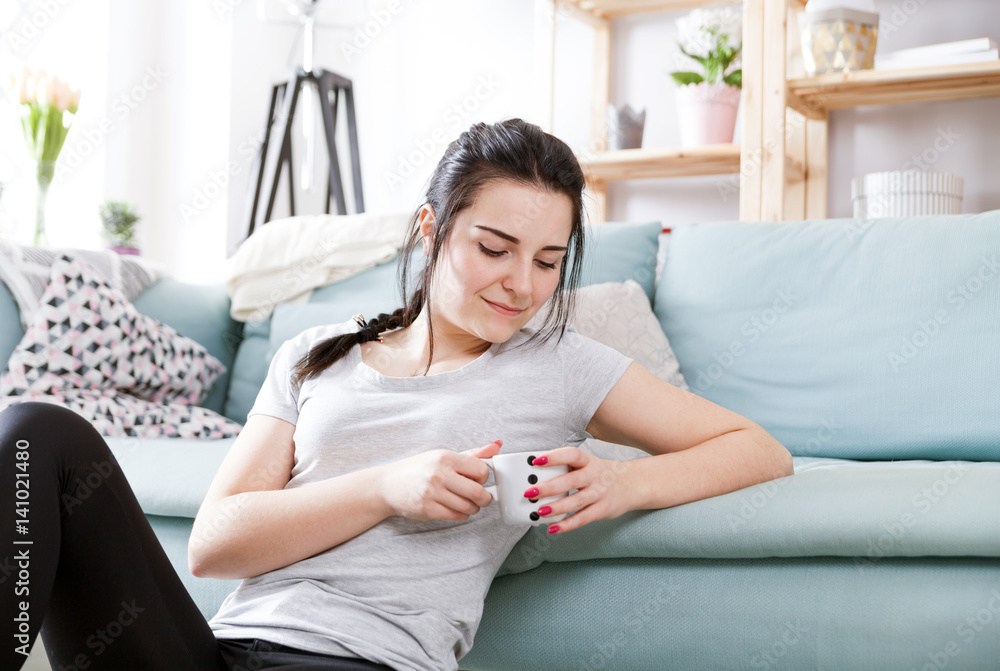 Young relaxed woman drinking coffee while sitting near comfortable sofa