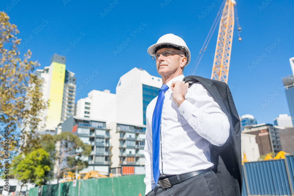 Senior elegant builder man in suit at construction site on sunny summer day