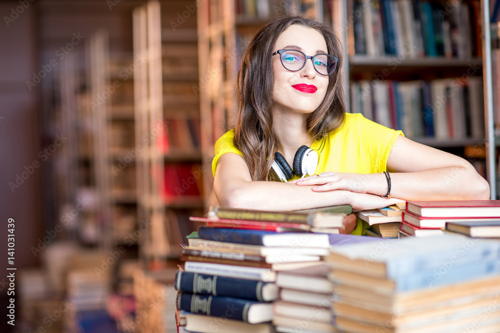 Portrait of young enthusiastic female student studying with a lot of books at the library