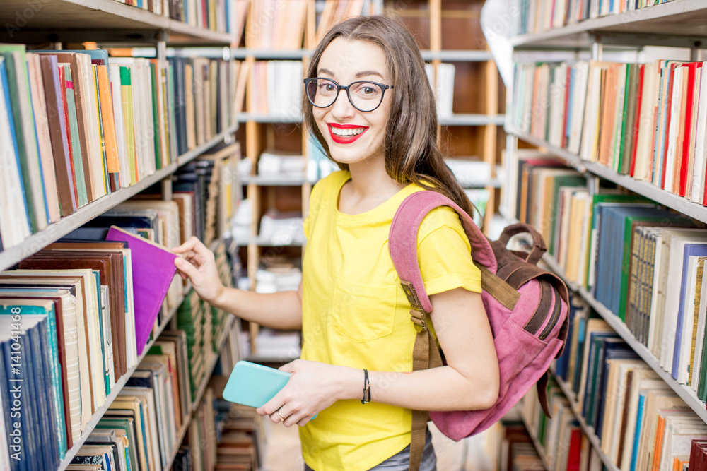 年轻、快乐、热情的女学生在图书馆书架上找书