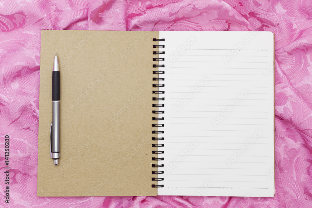 Blank notebook with pen on pink silk or clothes texture can use design and background.