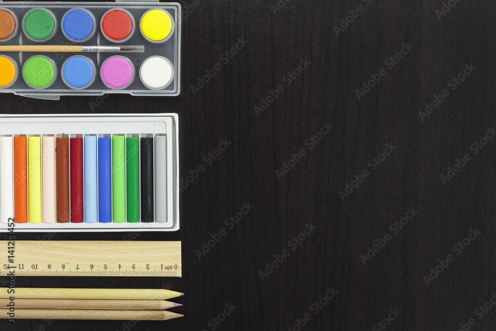 palette with paint and brush,pencil,ruler,colorful chalk on dark black wooden table background.