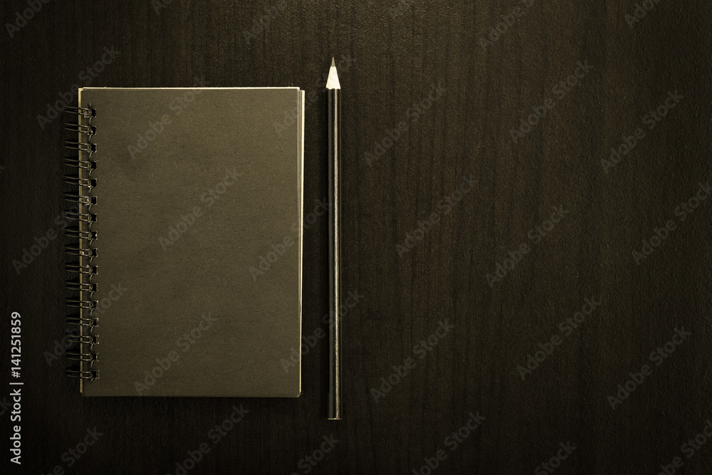 Black blank notebook with pencil on dark chalkboard background.