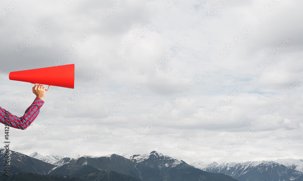 Hand of woman holding paper trumpet against natural landscape background